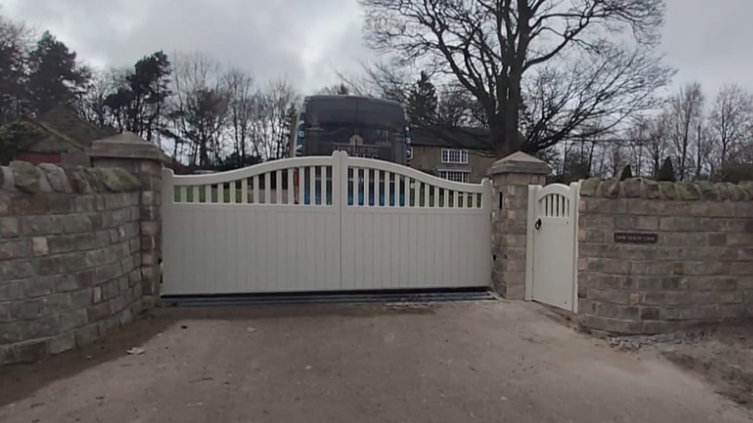 Cream painted timber double gate between stone pillars on a gravel drive