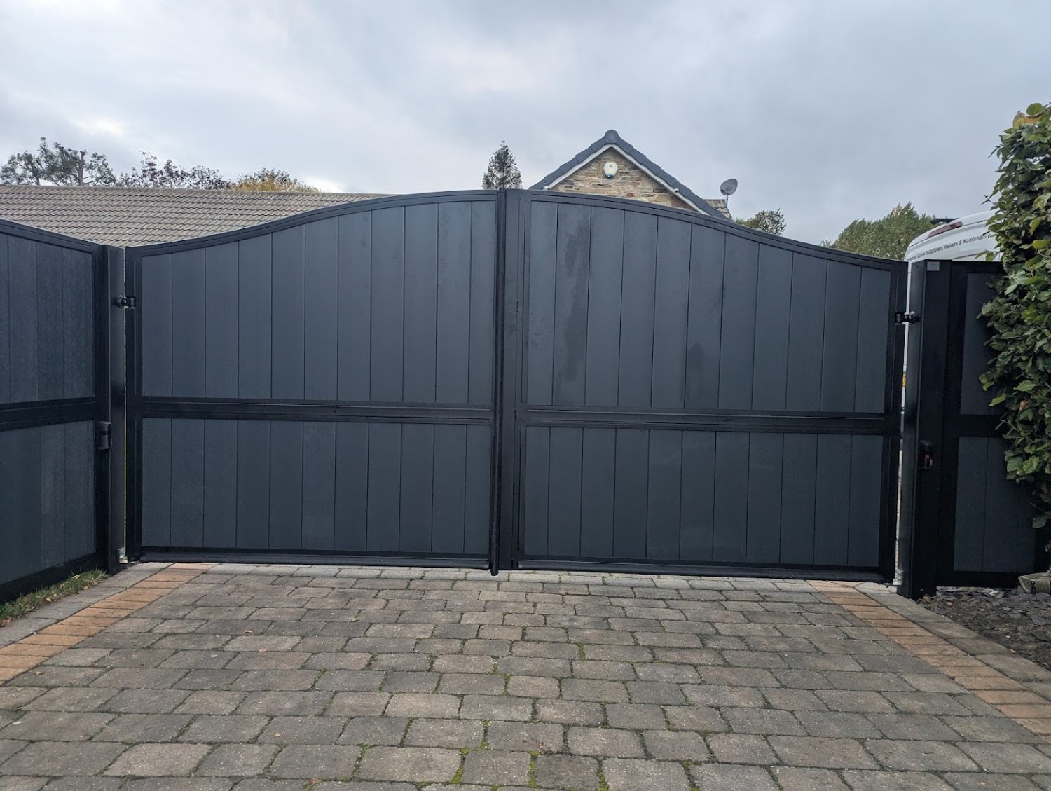 A charcoal composite bell-top double gate closed across a block-paved drive